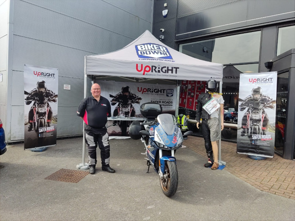 Man standing next to motorbike under 'UpRight' marquee